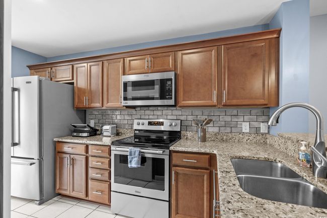 Kitchen with appliances with stainless steel finishes, a sink, brown cabinets, and light stone countertops | Image 8