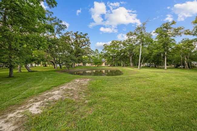 Charming water’s-edge perspective capturing the tranquil pond and verdant lawn, with the home peeking through the treeline beyond. | Image 37