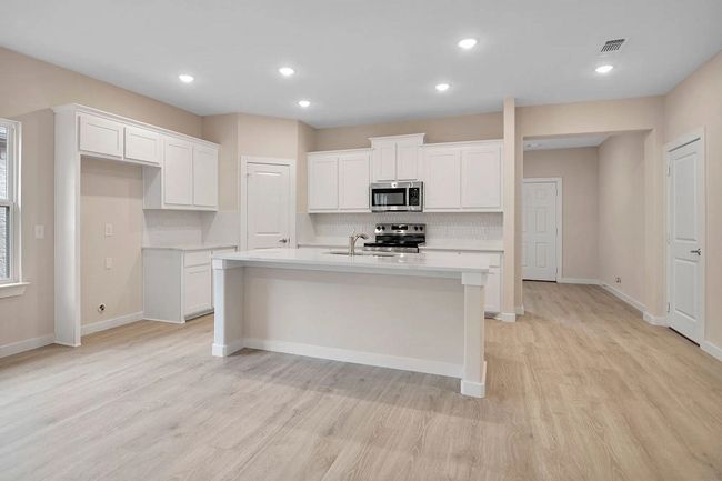 Kitchen with appliances with stainless steel finishes, light wood-style flooring, a center island with sink, light countertops, and tasteful backsplash | Image 8