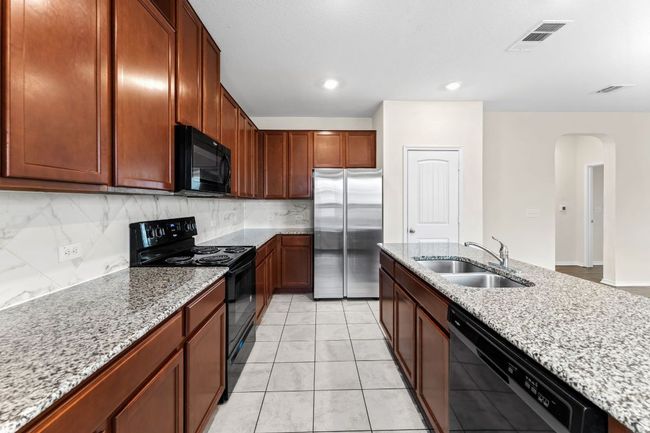 Kitchen featuring arched walkways, black appliances, light stone counters, decorative backsplash, and recessed lighting | Image 10