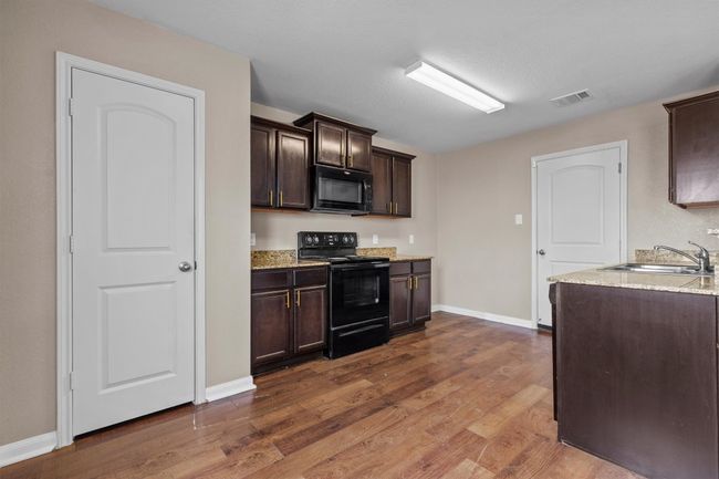 Kitchen with visible vents, a sink, dark brown cabinetry, and black appliances | Image 6