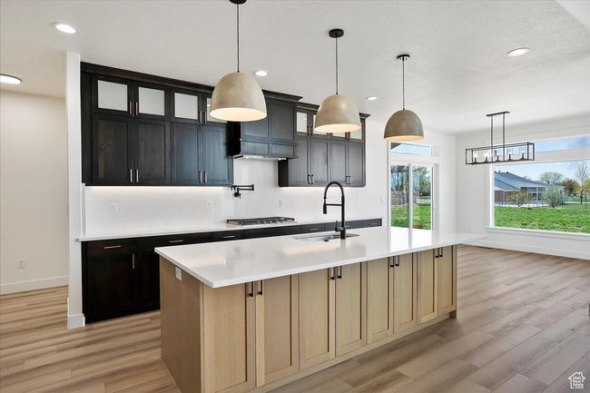 Kitchen featuring light wood-style flooring, a sink, baseboards, light countertops, and an island with sink | Image 6