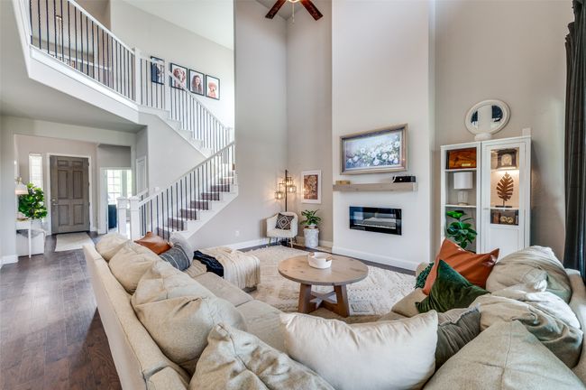 Living room with a towering ceiling, a glass covered fireplace, stairway, wood finished floors, and baseboards | Image 6