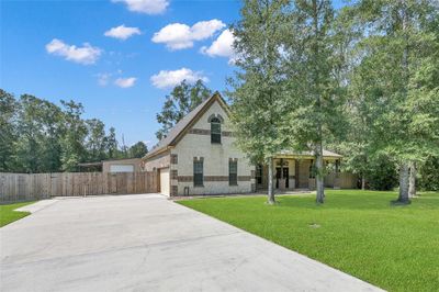 This is a two-story brick home with a spacious driveway, nestled among mature trees, featuring a covered entrance and a fenced backyard for privacy. | Image 2