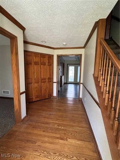 Hallway featuring a textured ceiling, crown molding, and dark wood-type flooring | Image 2