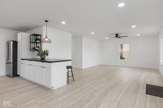 kitchen with light wood-style floors, freestanding refrigerator, a kitchen breakfast bar, white cabinets, and dark countertops | Image 34