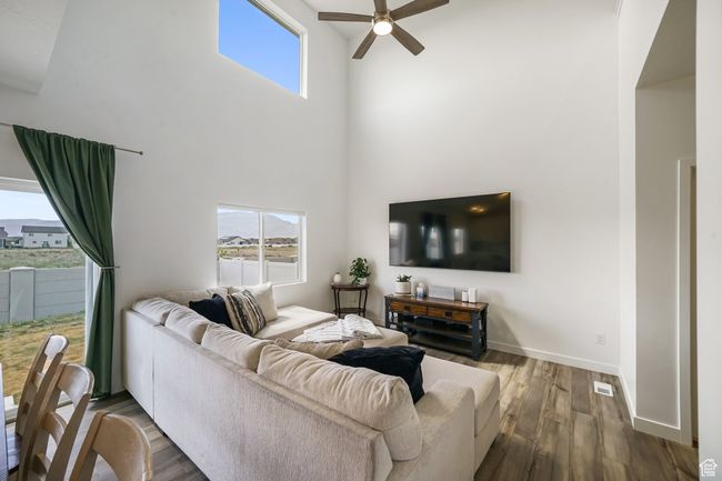 Living room with ceiling fan, a high ceiling, wood finished floors, healthy amount of natural light, and baseboards | Image 9
