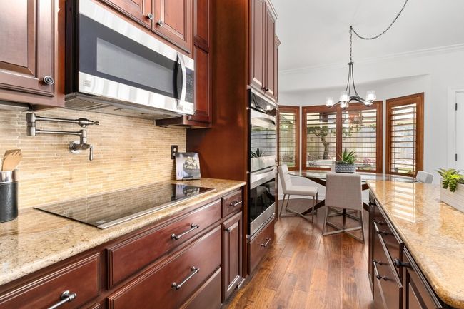 Kitchen featuring appliances with stainless steel finishes, dark wood-style floors, decorative backsplash, dark brown cabinets, and pendant lighting | Image 11