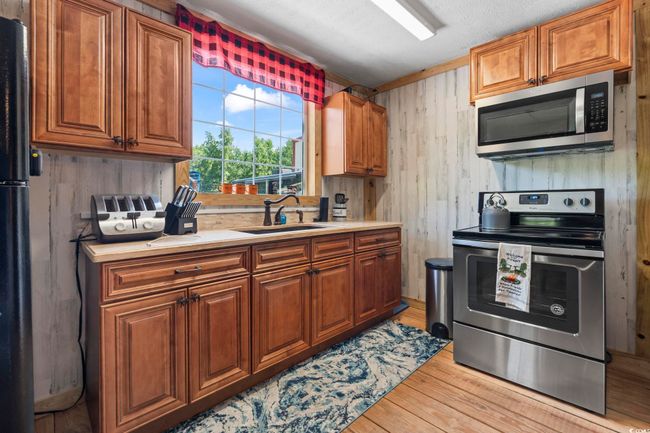 Kitchen with stainless steel appliances, light countertops, light wood-style flooring, wood walls, and brown cabinetry | Image 11