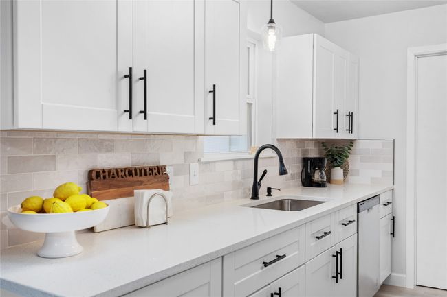 Kitchen featuring a sink, white cabinetry, backsplash, dishwasher, and decorative light fixtures | Image 10