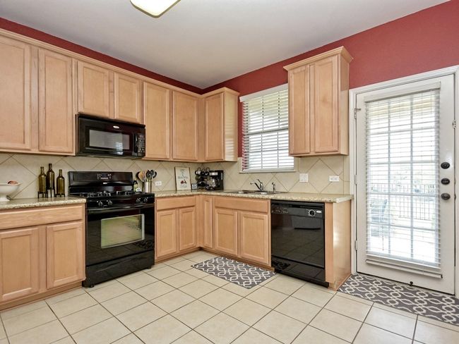 Kitchen with black appliances, backsplash, light brown cabinetry, and a sink | Image 11