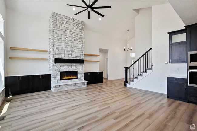 Unfurnished living room featuring light wood-style flooring, ceiling fan with notable chandelier, a high ceiling, stairway, and a fireplace | Image 4