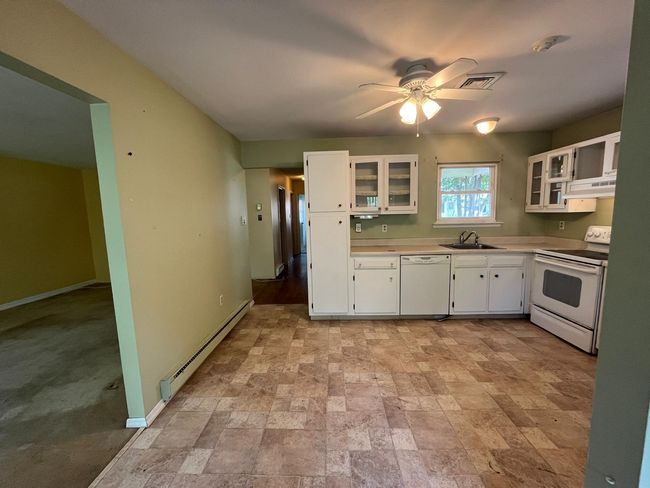 Kitchen featuring white appliances, a sink, under cabinet range hood, a baseboard heating unit, and ceiling fan | Image 4