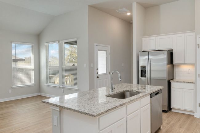 Kitchen with decorative backsplash, light wood-style flooring, appliances with stainless steel finishes, white cabinetry, and a sink | Image 16