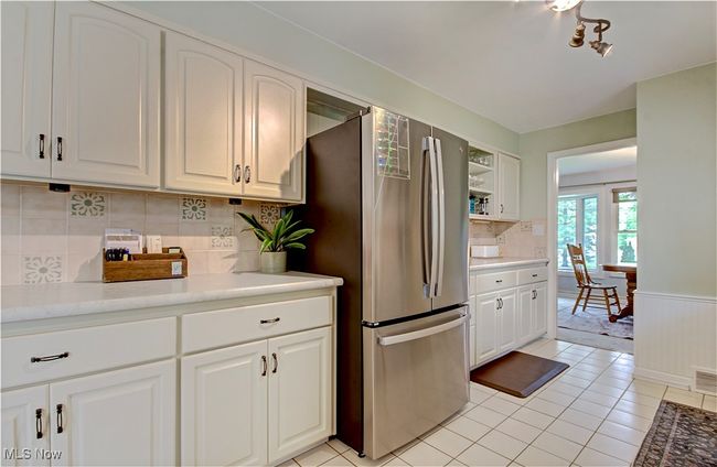 Kitchen featuring freestanding refrigerator, white cabinetry, light tile patterned flooring, wainscoting, and backsplash | Image 16