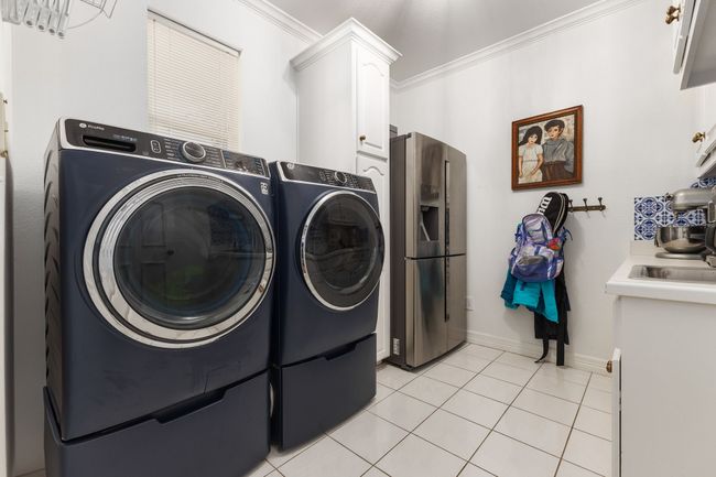 Laundry room featuring light tile patterned floors, baseboards, cabinet space, washer and clothes dryer, and crown molding | Image 28