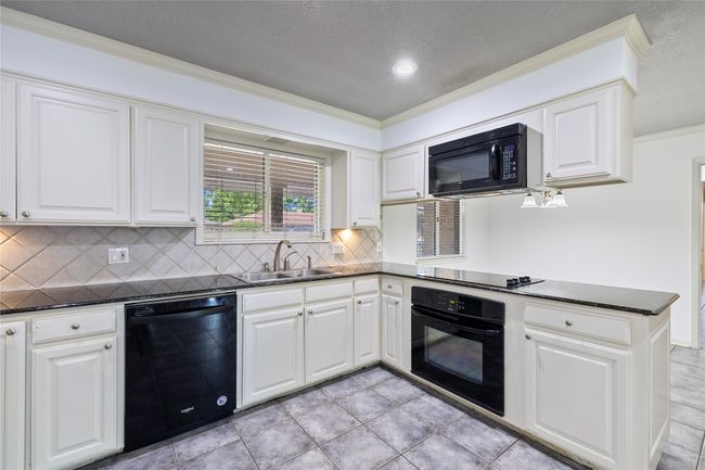 Kitchen featuring black appliances, a sink, backsplash, a peninsula, and crown molding | Image 9