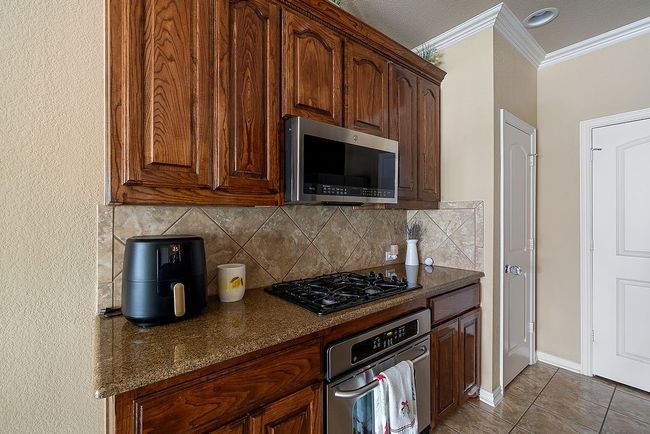 Kitchen featuring dark stone countertops, stainless steel appliances, ornamental molding, backsplash, and baseboards | Image 32