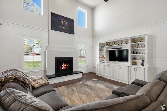Living area with a lit fireplace, a towering ceiling, dark wood-style floors, and plenty of natural light | Image 9