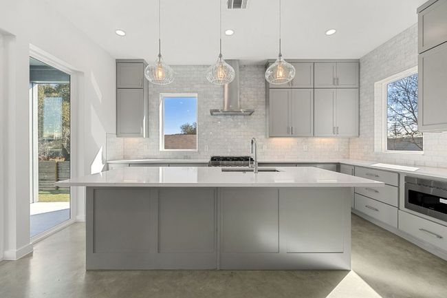 Kitchen with concrete floors, a sink, range hood, gray cabinets, and stainless steel microwave | Image 6
