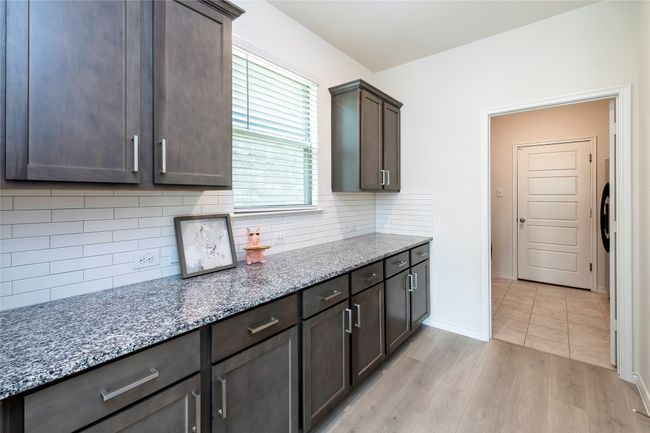 Kitchen featuring light stone counters, light wood finished floors, dark brown cabinetry, and tasteful backsplash | Image 11