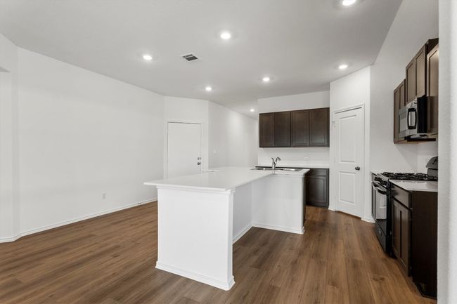 Kitchen with black appliances, dark wood-style floors, a kitchen island with sink, light countertops, and dark brown cabinetry | Image 7
