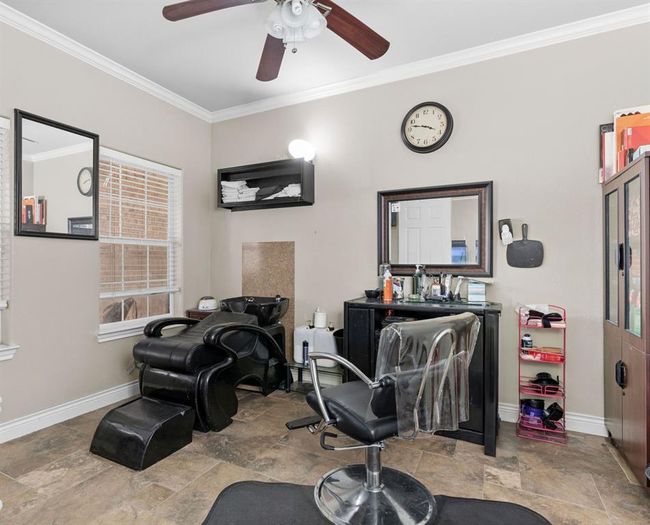 This room is currently set up as a hair salon, featuring two styling chairs, mirrors, a wash station, and storage units. It has tiled flooring, neutral wall colors, and good natural light from a window. A ceiling fan provides additional comfort. | Image 43