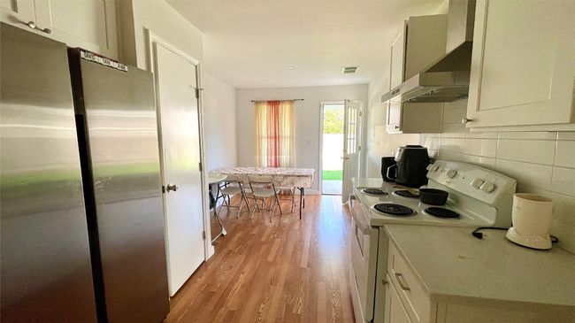 Kitchen with freestanding refrigerator, white electric stove, ventilation hood, light wood-type flooring, and tasteful backsplash | Image 19