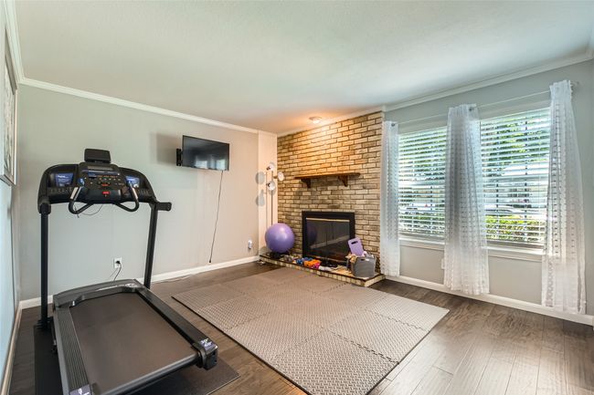 Workout room featuring baseboards, ornamental molding, wood finished floors, and a brick fireplace | Image 10
