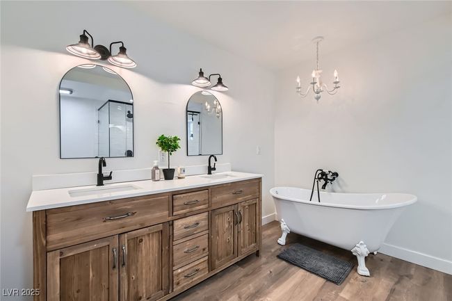 Bathroom featuring double vanity, wood finished floors, a freestanding tub, a chandelier, and baseboards | Image 20