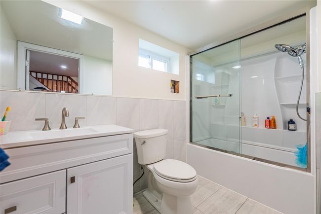 Bathroom with toilet, vanity, combined bath / shower with glass door, tile walls, and a wainscoted wall | Image 35