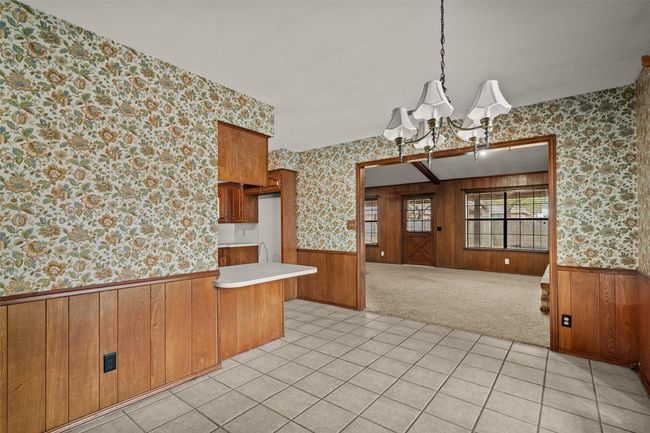 Kitchen with light countertops, wainscoting, wallpapered walls, brown cabinetry, and a notable chandelier | Image 11