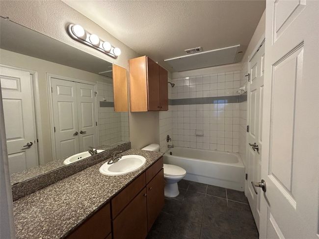 Full bath featuring toilet, a textured ceiling, shower / tub combination, vanity, and tile patterned flooring | Image 16