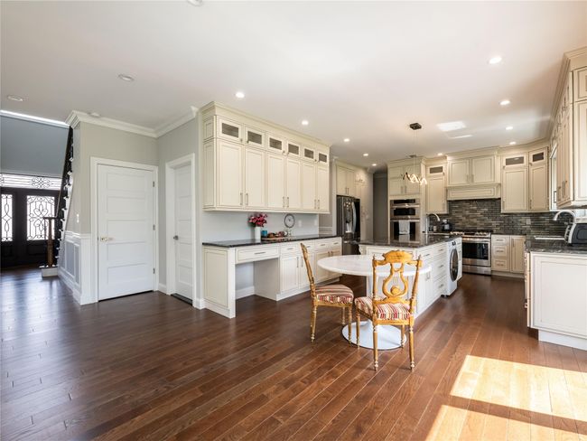 Kitchen featuring a center island, dark wood finished floors, glass insert cabinets, appliances with stainless steel finishes, and ornamental molding | Image 8