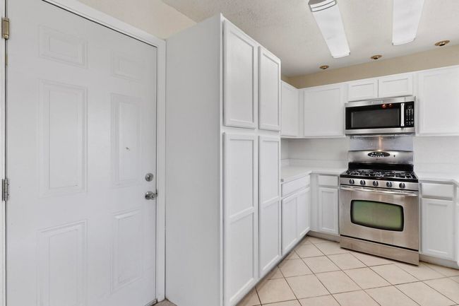 Kitchen with appliances with stainless steel finishes, light countertops, white cabinets, and light tile patterned flooring | Image 13
