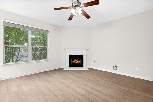 Unfurnished living room with wood finished floors, a warm lit fireplace, and ceiling fan | Image 8