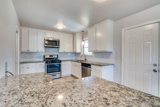 Kitchen with stainless steel appliances, backsplash, a sink, and light stone counters | Image 12
