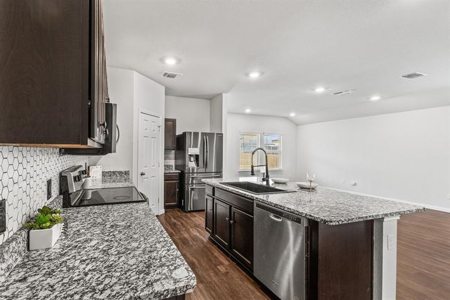 Kitchen with appliances with stainless steel finishes, dark brown cabinets, dark wood finished floors, a center island with sink, and backsplash | Image 7