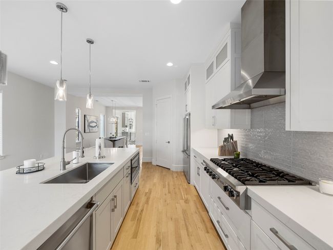 Kitchen featuring wall chimney range hood, stainless steel appliances, light countertops, backsplash, and light wood-type flooring | Image 14
