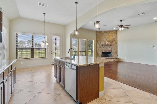 Kitchen with light tile patterned flooring, ceiling fan, stainless steel dishwasher, a stone fireplace, and light stone counters | Image 22