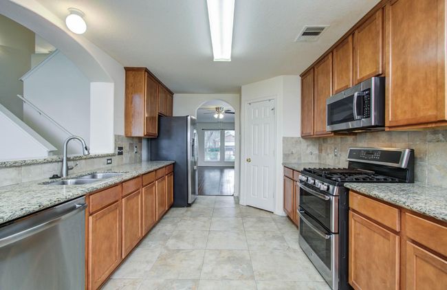 The kitchen has oversized tile flooring, decorative backsplash, and granite countertops. | Image 10