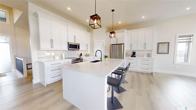 Kitchen with stainless steel appliances, light wood-style floors, a breakfast bar area, an island with sink, and light countertops | Image 8