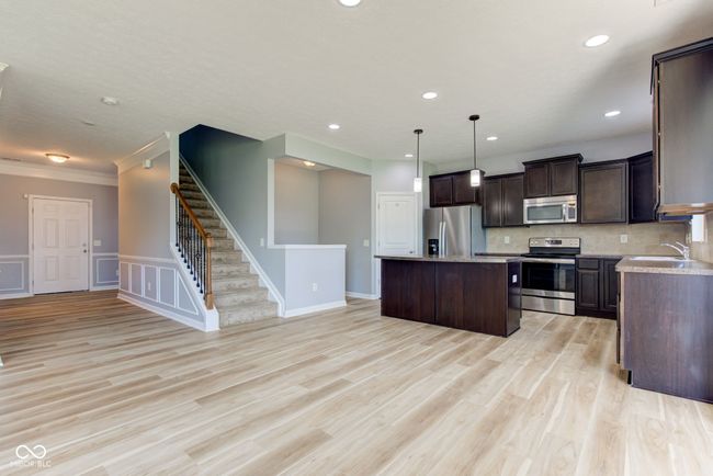kitchen with appliances with stainless steel finishes, a kitchen island, dark brown cabinetry, light countertops, and light wood-type flooring | Image 13