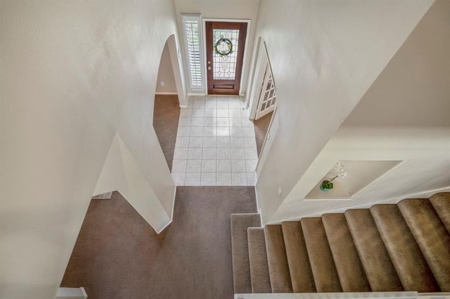 Moving upstairs, this view down over the bannister offers a clear look at the front foyer. The front door is framed between the doorways leading to the formal dining room and study, while a decorative art niche in the wall along the staircase adds a touch of character directly below. | Image 24