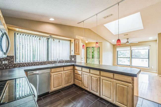Kitchen featuring tasteful backsplash, lofted ceiling with skylight, a peninsula, tile countertops, and dishwasher | Image 16