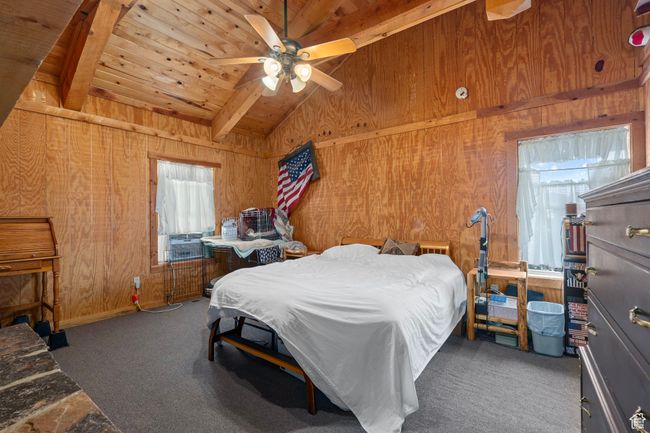 Carpeted bedroom with cooling unit, ceiling fan, wooden ceiling, vaulted ceiling with beams, and wood walls and through fireplace to living room | Image 14