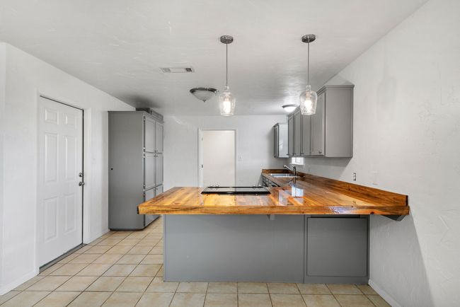 Kitchen with gray cabinetry, wooden counters, a peninsula, and black electric stovetop | Image 8