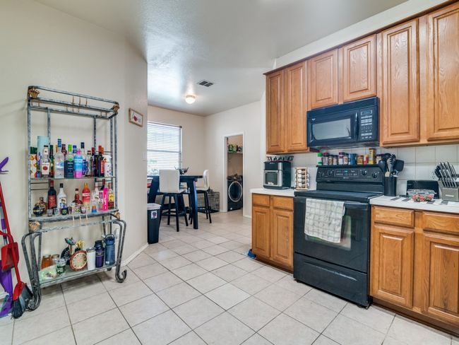 Kitchen with black appliances, light tile patterned floors, washer / clothes dryer, and light countertops | Image 10