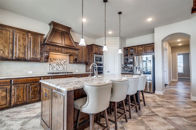 Kitchen featuring tasteful backsplash, a kitchen island with sink, stainless steel appliances, light stone countertops, and custom range hood | Image 14