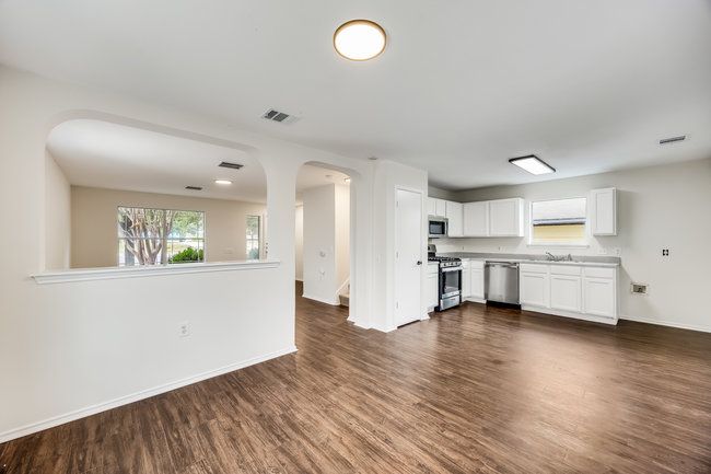 Unfurnished living room featuring arched walkways, healthy amount of natural light, dark wood-type flooring, and baseboards | Image 11